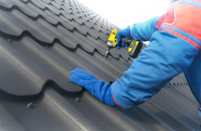 Man worker uses a power drill to attach a cap metal roofing job with screws.
